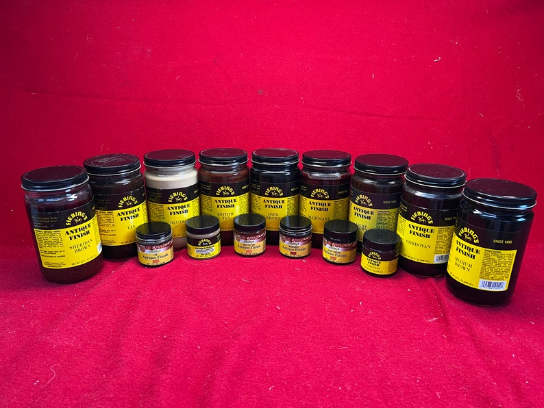 May include: A collection of 14 bottles of Fiebing's Antique Finish leather dye in various colors, including Saddle Brown, Tan, Neutral, Bitter Tan, Dark, Mahogany, Black, Cordouan, and Red Oak Brown. The bottles are arranged in a row on a red surface.