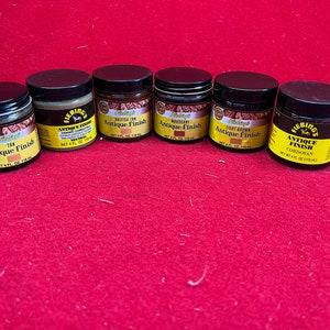 May include: Six small jars of Fiebing's Antique Finish leather dye in various colors, including British Tan, Mahogany, Light Brown, and Cordovan. Each jar is labeled with the Fiebing's logo and the color name.