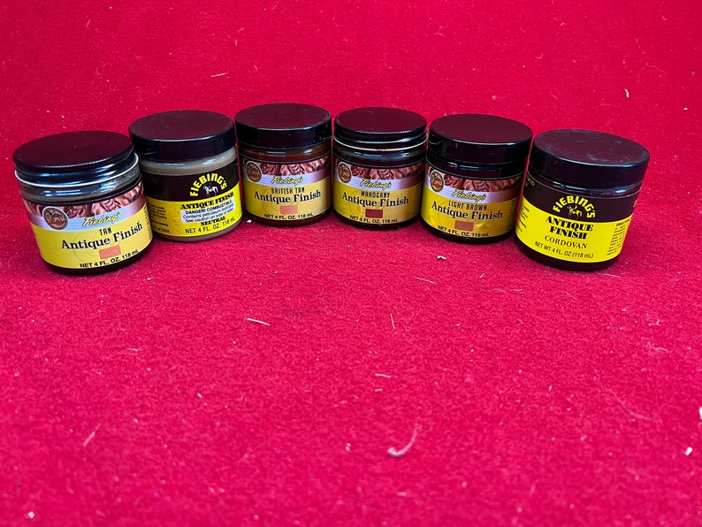 May include: Six small jars of Fiebing's Antique Finish leather dye in various colors, including British Tan, Mahogany, Light Brown, and Cordovan. Each jar is labeled with the Fiebing's logo and the color name.
