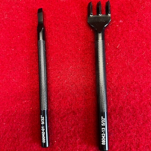 May include: Two black leather working tools on a red surface. The tool on the left is a stitching awl with the number "88042-01 5/32" printed on it. The tool on the right is a stitching pricker with the number "88042-13 5/32" printed on it.