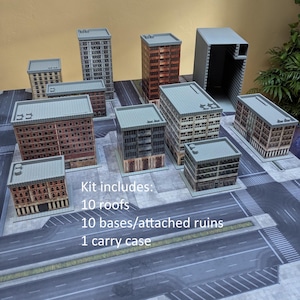 May include: A collection of miniature city buildings arranged on a printed street mat. The kit includes 10 roofs, 10 bases/attached ruins, and 1 carry case. The structures feature various architectural designs with brick and concrete textures.