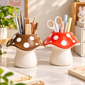 May include: Two mushroom-shaped desk organizers with cream-colored stems and wide caps. One cap is brown with white spots, holding pencils and erasers. The other cap is red with white spots, holding scissors and pens. Both are functional containers.