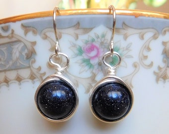May include: A pair of silver dangle earrings with dark blue, sparkly, round stones.