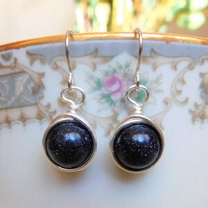 May include: A pair of silver dangle earrings with dark blue, sparkly, round stones.
