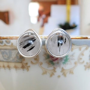 May include: A pair of silver wire wrapped earrings with black and white rutilated quartz stones.