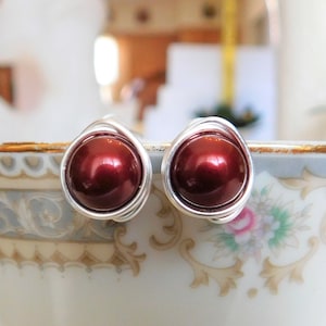 May include: A pair of silver wire wrapped earrings with dark red pearl beads.