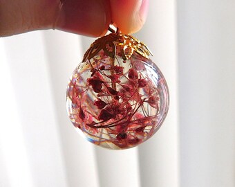 May include: A clear glass sphere pendant with a gold metal bail. Inside the sphere are dried red flowers and stems.