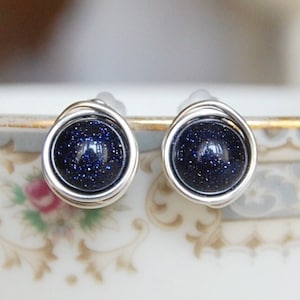 May include: A pair of silver wire wrapped earrings with blue glitter stone cabochons.