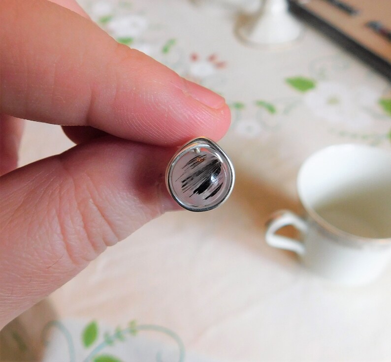 May include: A silver ring with a round, clear stone that has black and white streaks. The stone is set in a silver bezel.