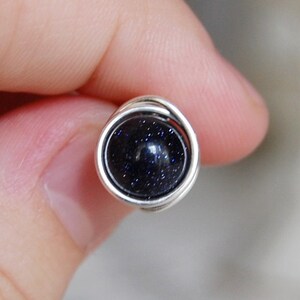 May include: A silver wire wrapped ring with a dark blue gemstone. The gemstone has a speckled texture.