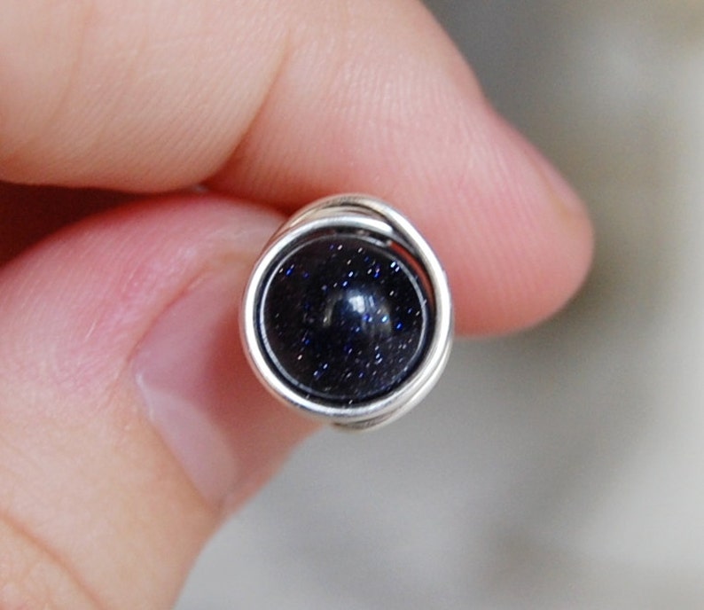 May include: A silver wire wrapped ring with a dark blue gemstone. The gemstone has a speckled texture.