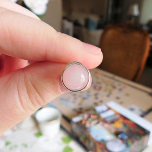 May include: A silver ring with a round, light pink gemstone.