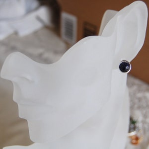 May include: A close-up of a silver stud earring with a dark blue gemstone. The earring is displayed on a white mannequin head.