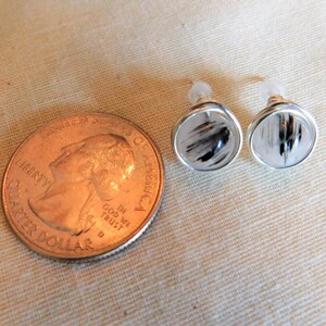 May include: A pair of silver earrings with clear quartz stones and black inclusions. The earrings are about the size of a US quarter.