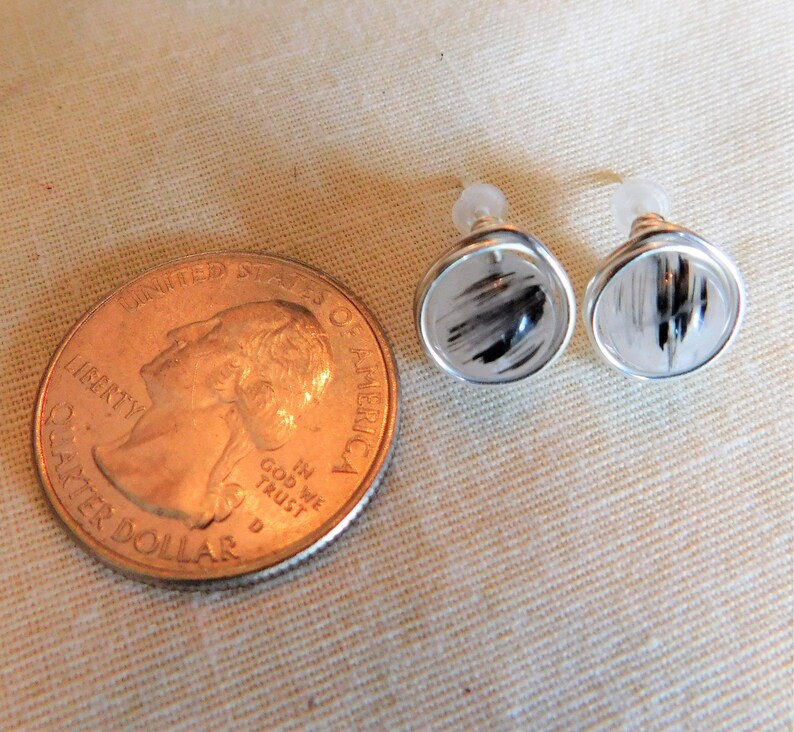 May include: A pair of silver earrings with clear quartz stones and black inclusions. The earrings are about the size of a US quarter.