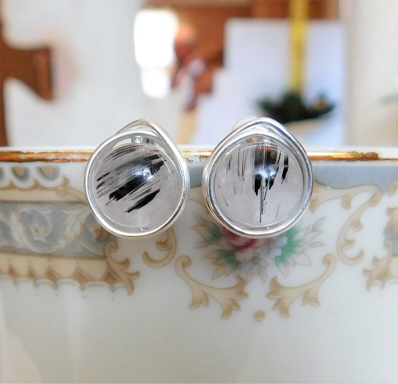 May include: A pair of silver wire wrapped earrings with black and white rutilated quartz stones.