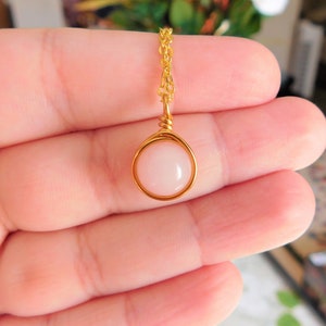 May include: A delicate gold chain necklace with a pink gemstone pendant. The pendant is set in a gold wire frame.