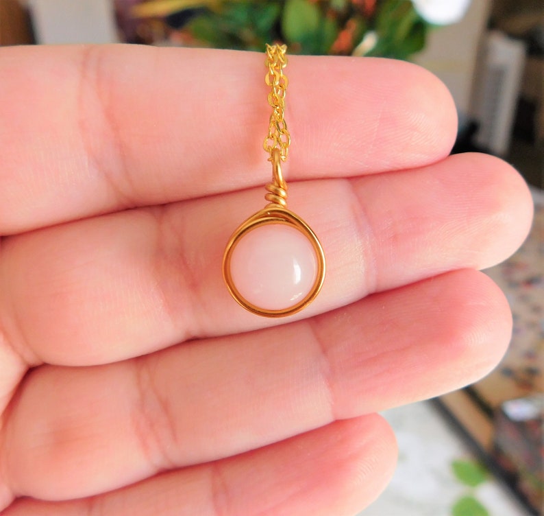 May include: A delicate gold chain necklace with a pink gemstone pendant. The pendant is set in a gold wire frame.