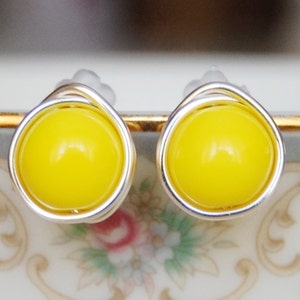 May include: A pair of yellow stud earrings with silver wire wrapping. The earrings are on a white surface with a floral pattern.