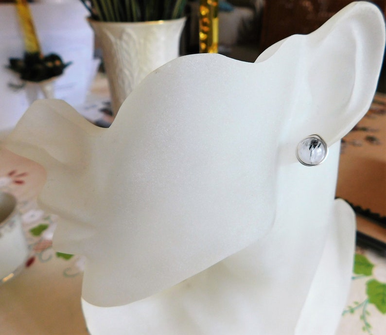 May include: A white ceramic mannequin head with a single silver earring featuring a clear crystal stone.