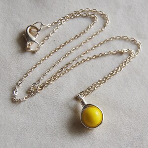 May include: A silver chain necklace with a yellow glass pendant. The pendant is wrapped in silver wire.