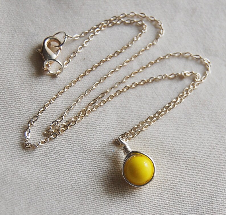 May include: A silver chain necklace with a yellow glass pendant. The pendant is wrapped in silver wire.