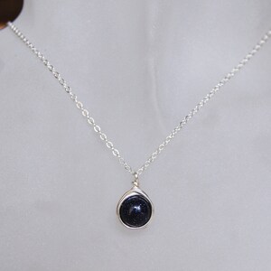 May include: A silver chain necklace with a dark blue gemstone pendant. The pendant is wrapped in silver wire.
