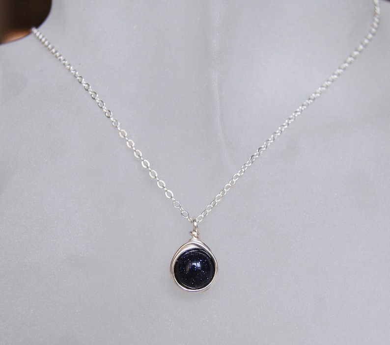 May include: A silver chain necklace with a dark blue gemstone pendant. The pendant is wrapped in silver wire.