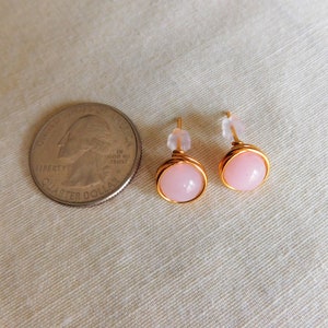 May include: A pair of gold wire wrapped earrings with pink stone accents. The earrings are shown next to a US quarter for size reference.