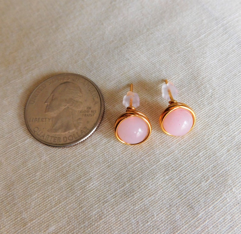 May include: A pair of gold wire wrapped earrings with pink stone accents. The earrings are shown next to a US quarter for size reference.