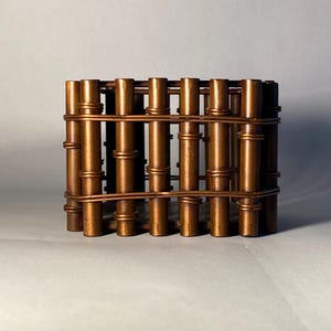 May include: A square-shaped container constructed from vertical brown cylindrical rods that resemble bamboo stalks. The rods are held together by horizontal copper-colored wire bands wrapped around the exterior at the top and bottom sections.
