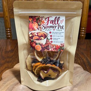 Può includere: Una busta beige contenente fette di arancia essiccate, fette di mela e chiodi di garofano interi. L'etichetta riporta la scritta Fall Simmer Pot con le istruzioni per aggiungere il contenuto in un pentolino, 3-4 tazze d'acqua e cuocere a fuoco lento.