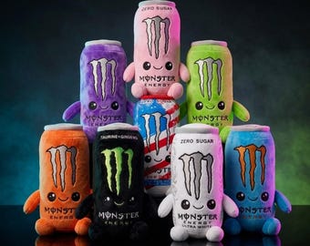 Peut inclure: Une collection de peluches en forme de canettes de boisson Monster Energy de différentes couleurs, dont rose, violet, vert, orange, noir, blanc et bleu, chacune avec un visage souriant, de petits bras et le logo Monster Energy imprimé.