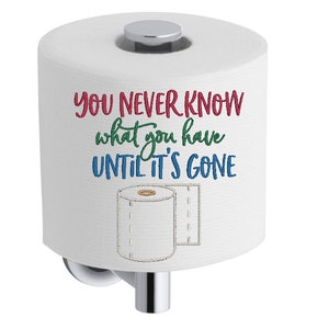 Pode incluir: Rolo de papel higiênico branco com uma tampa prateada e um suporte. O papel higiênico tem um design bordado que diz "You never know what you have until it's gone".