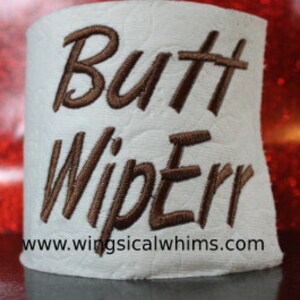 May include: A white toilet paper roll with brown embroidery that reads "Butt Wiperr" and a website address.