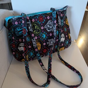 Puede incluir: Bolso tote negro con un colorido estampado de Star Wars. El bolso presenta im&aacute;genes de Stormtroopers, Darth Vader y otros personajes ic&oacute;nicos. El interior est&aacute; forrado con una tela azul brillante y el bolso tiene asas a juego.