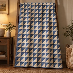 May include: A rectangular quilt featuring a repeating geometric pattern of blue and off-white triangles arranged in a grid. The fabric displays visible stitching lines throughout the surface, creating a textured appearance across the entire piece.