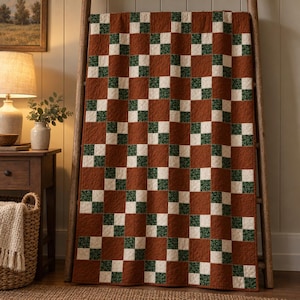May include: A quilt featuring a repeating checkerboard pattern of solid rust-colored squares, cream-colored squares, and dark green squares with a small white floral print. The fabric has a visible quilted texture throughout the entire surface.