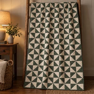 May include: A rectangular quilt featuring a repeating geometric pattern of dark green floral print triangles and solid cream-colored triangles. The quilt is draped over a wooden ladder, showcasing a consistent grid of squares composed of four triangles.