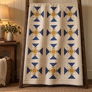 May include: A rectangular quilt featuring a repeating geometric block pattern in cream, mustard yellow, and navy blue with a small floral print. The quilt is draped over a wooden ladder, showcasing visible grid stitching across the fabric surface.