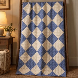 May include: A quilted blanket featuring a repeating diamond pattern of alternating solid cream-colored squares and blue squares with a small white floral print. The quilt is draped over a wooden ladder, showcasing visible grid-like stitching.