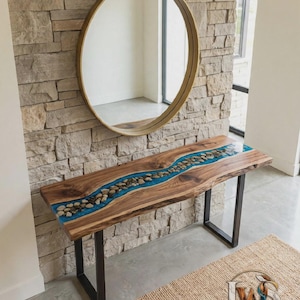 May include: A console table featuring a live-edge wood slab with a central river-like inlay of blue resin and embedded river stones, supported by two black metal U-shaped legs. The logo LuxeWoodNStone is visible in the bottom right corner.