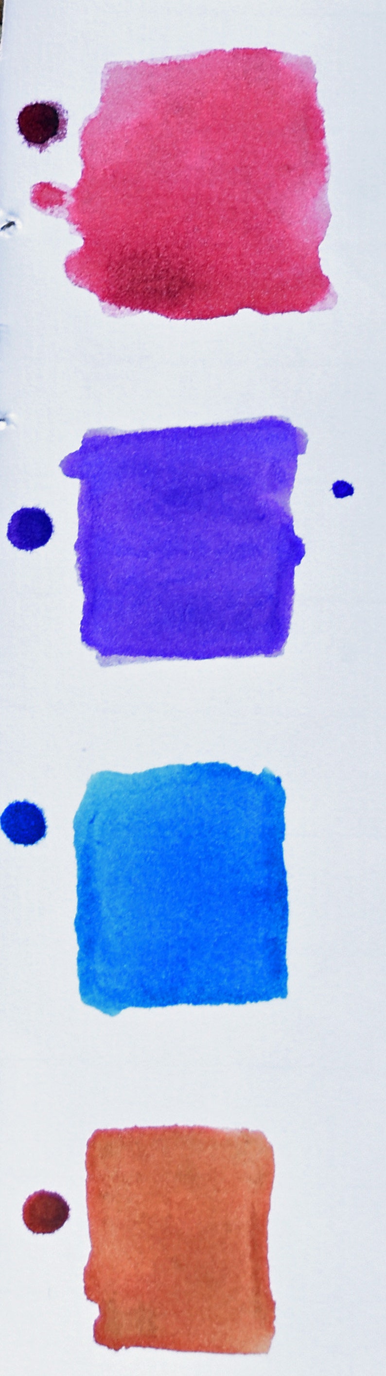 K&ouml;nnte beinhalten: Ein vertikales Bild zeigt vier rechteckige Aquarellfarbfelder in Rot, Lila, Blau und Orange, jeweils mit einem Punkt. Die Farbfelder befinden sich auf wei&szlig;em Hintergrund, was auf eine Farbpalette oder eine Demonstration von Kunstbedarf hindeutet.