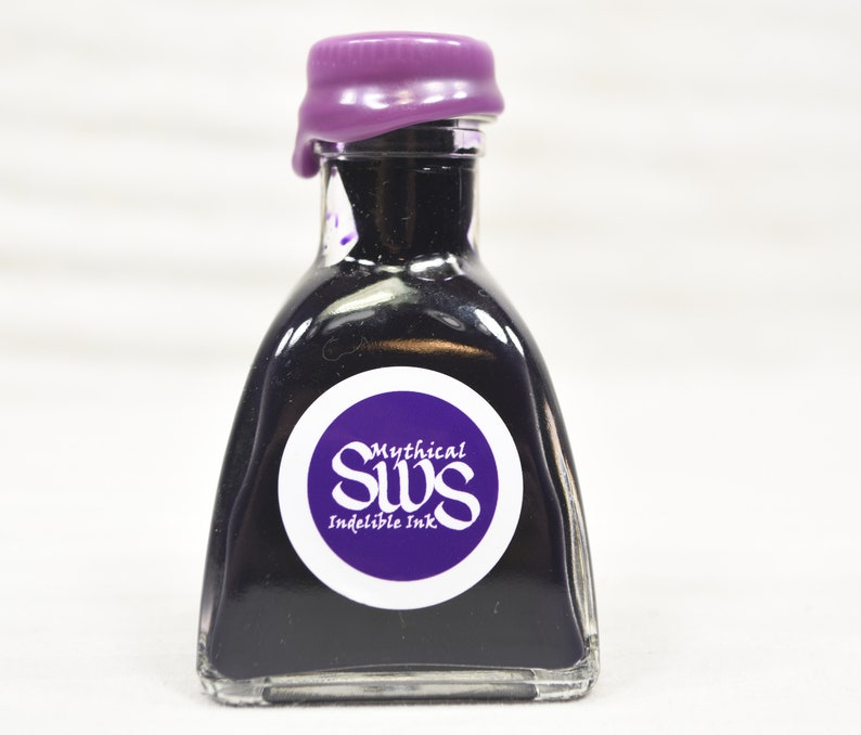 K&ouml;nnte beinhalten: Kleine, klare Glasflasche gef&uuml;llt mit tiefvioletter Tinte. Die Flasche hat einen lila Wachsverschluss und ein rundes Etikett mit dem wei&szlig;en Text "Mythical SWS Indelible Ink". Geeignet f&uuml;r Kalligraphie.