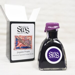 K&ouml;nnte beinhalten: Eine Flasche Gryphon Purple F&uuml;llfederhalter-Tinte mit einem lila Wachssiegel. Die Flasche hat ein wei&szlig;es Etikett mit dem Text "Mythical SWS Indelible Ink". Eine schwarze Schachtel mit dem gleichen Logo und einer Zeichnung einer mythischen Kreatur befindet sich daneben.