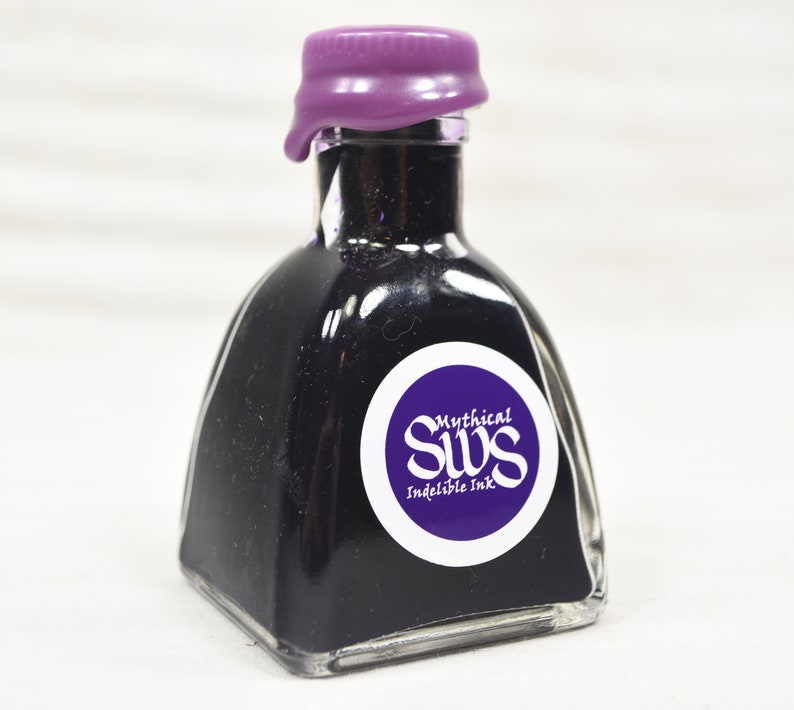 K&ouml;nnte beinhalten: Eine kleine, quadratische Glasflasche gef&uuml;llt mit dunkelvioletter Tinte. Die Flasche hat ein lilafarbenes Wachssiegel und ein wei&szlig;es Etikett mit dem Text "Mythical SWS Indelible Ink" in einem kreisf&ouml;rmigen Design. Die Tinte ist durch das klare Glas sichtbar.