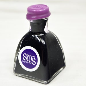 K&ouml;nnte beinhalten: Kleine, klare Glas-Tintenflasche gef&uuml;llt mit dunkelvioletter Tinte. Die Flasche hat einen lila Verschluss und ein wei&szlig;es und lila Etikett mit der Aufschrift "Mythical SWS Indelible Ink". Die Flasche hat eine einzigartige, quadratische Form.