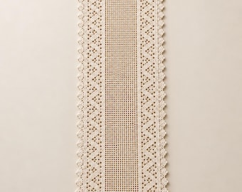 May include: A rectangular cream-colored crochet table runner featuring a central grid pattern flanked by intricate zigzag borders and a scalloped edge. The textile displays a consistent open-weave design throughout the entire piece.