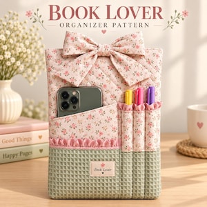 May include: A quilted fabric book organizer featuring a pink floral pattern on the top half and a sage green waffle-textured fabric on the bottom. It includes a large bow, a smartphone pocket, and three pen slots with a Book Lover label.