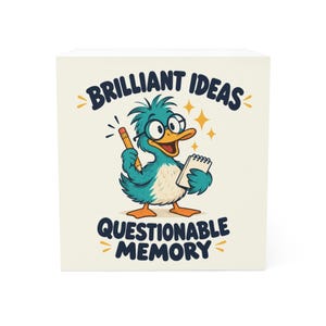 May include: A square white notepad featuring a cartoon teal duck wearing black glasses, holding a yellow pencil and a small notebook. The text reads BRILLIANT IDEAS above the duck and QUESTIONABLE MEMORY below in dark blue lettering.